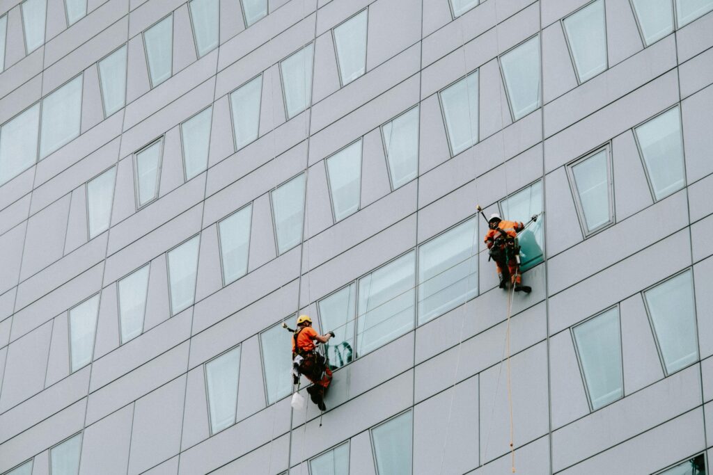 Dos profesionales de una empresa de limpieza limpiando ventanas y cristales colgados con cuerdas en altura, utilizando equipo especializado.